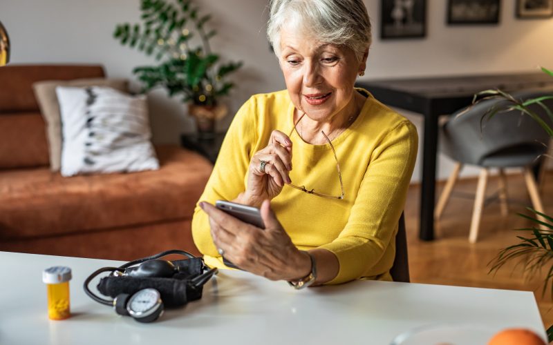 Senior woman at home preparing to drink medical pill. She is holding a pill bottle and looking at smart phone